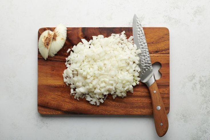 chopped onions on a cutting board with a knife next to it and an onion wedge