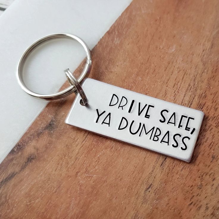 An adorable gift for any dumbass in your life! Perfect for your little brother or sister that just started driving. This keychain is so funny and will surely put a smile on the recipient's face! Item Details: Text on keychain: Drive Safe, Ya Dumbass Color: silverMetal: lightweight aluminumTag Size: 14 gauge, 5/8” x 1.5" Hardware: Stainless steel split ring, stainless steel key ring Options: - Keychain Only (main keychain tag only) - Add Name Charm (main keychain tag, plus round name charm) About this item:Keychains are stamped on 14 gauge aluminum. This is a preferred metal for many metal stampers. Aluminum is a very lightweight metal that will not rust, or tarnish. It is a lightweight metal, so it will not weigh down your key ring. Light scratching is normal with use and wear. Although it Car Gifts For Boyfriend, Car Gift Ideas, Funny Keychains, Funny Photos Ideas, Stocking Stuffers For Boys, Gifts For New Drivers, Funny Keychain, Teen Driver, Metal Stamped Jewelry