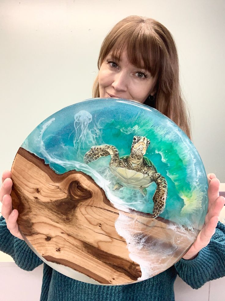 a woman holding up a plate with a painting of a turtle on it's back