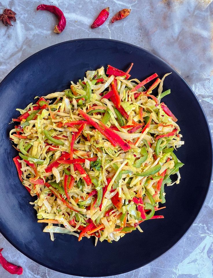 a black plate topped with coleslaw slaw and red bell peppers next to chilies