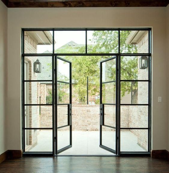 an open glass door leading to a brick building with trees in the backgroun