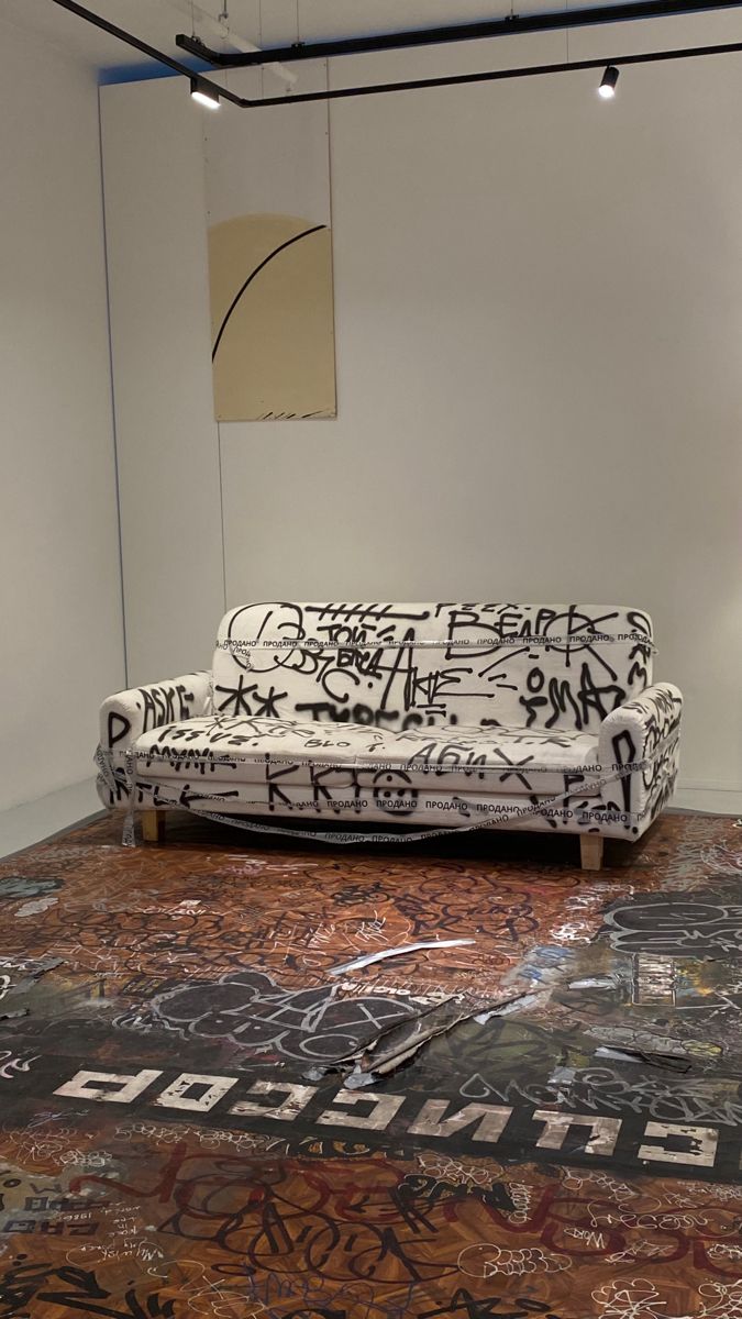 a couch covered in graffiti sitting on top of a floor next to a white wall