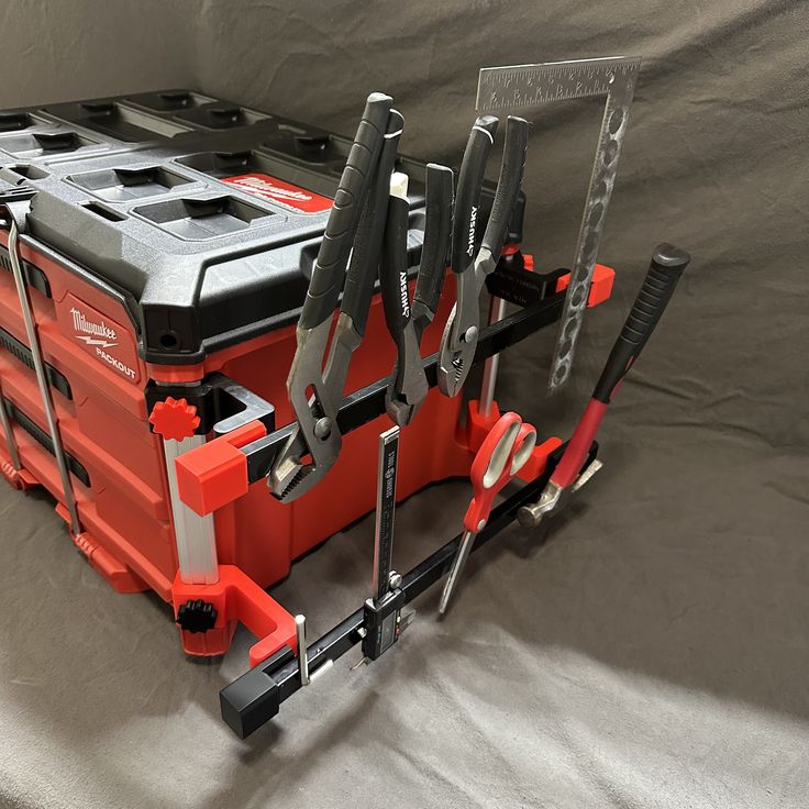 a tool box with tools attached to it on a gray cloth covered surface, in front of a grey background