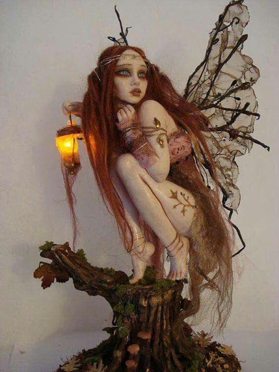 a statue of a fairy sitting on top of a tree stump next to a lamp