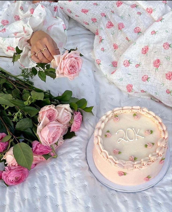 a cake and flowers on a bed next to a woman's hand holding a knife