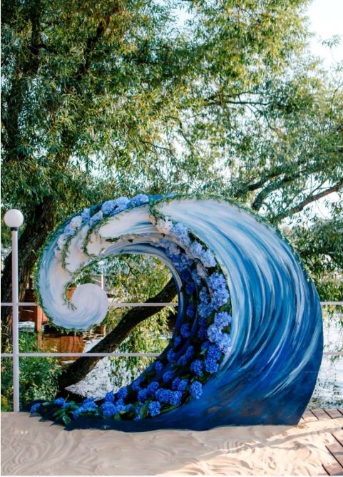 a sculpture made out of blue flowers in the shape of a wave on top of sand