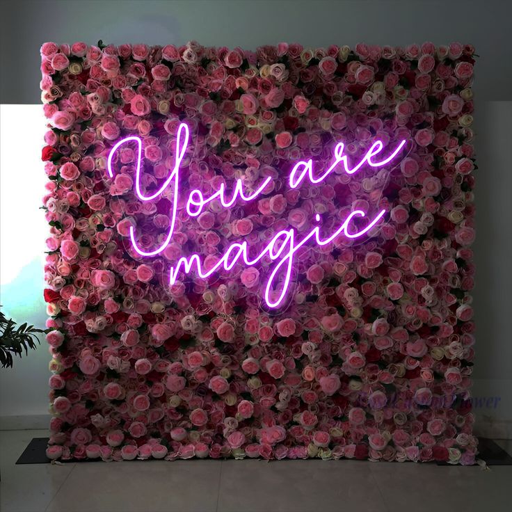 a pink flower wall with the words you are magic written in neon lights on it