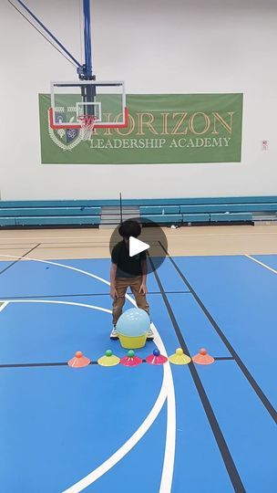 a person standing on top of a basketball court with an umbrella over their head and balls in front of them