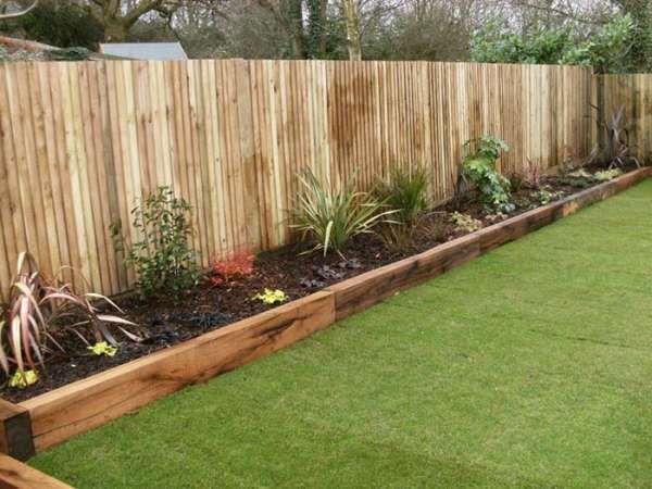 a wooden fence is next to a grassy area with flowers and plants in the middle