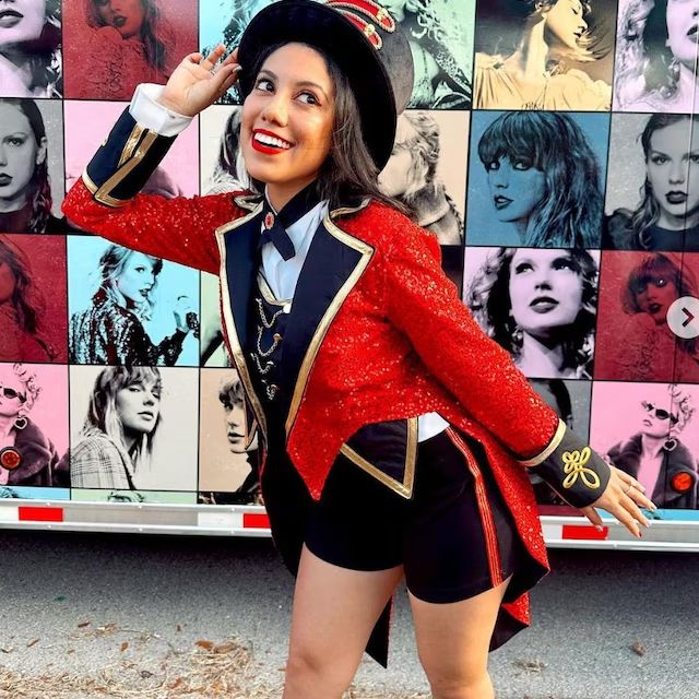 a woman in a red jacket and black shorts standing next to a wall with pictures on it