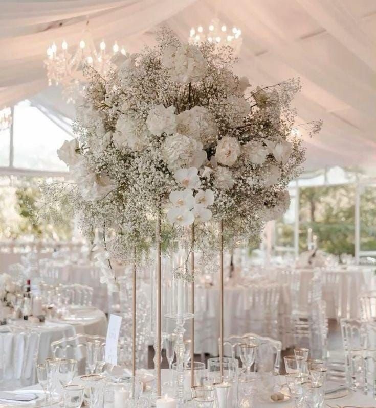 a tall vase filled with white flowers on top of a table covered in tables cloths