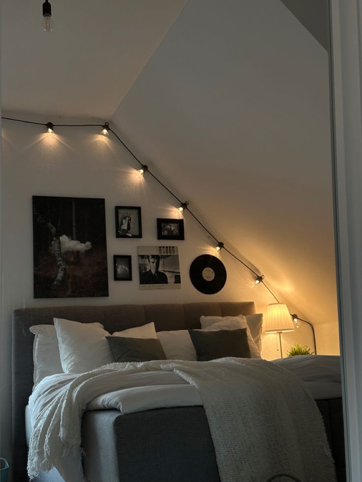 an attic bedroom with white walls and lights on the headboard, along with pictures above the bed