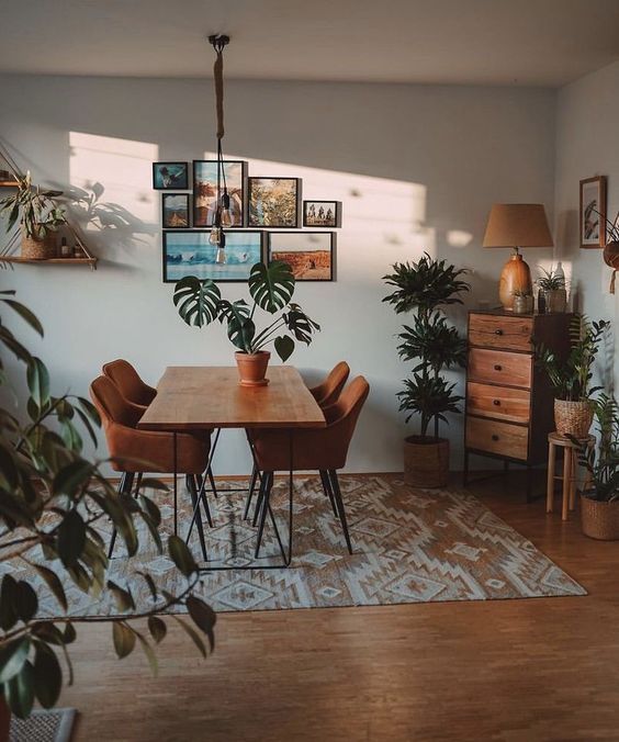 a dining room table surrounded by potted plants and pictures on the wall above it