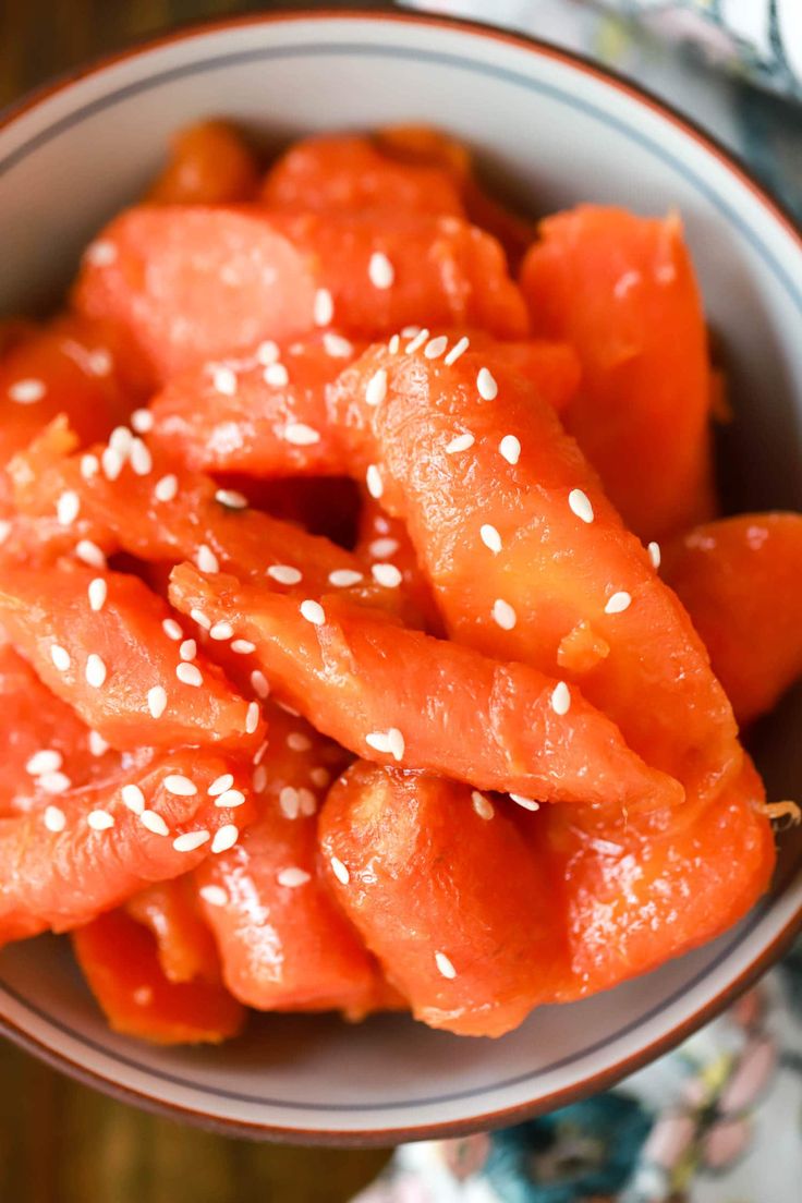 sweet carrots in a bowl with sesame seeds and sesame seeds on the side, text overlay reads my thai cook's sweet carrots for hibash