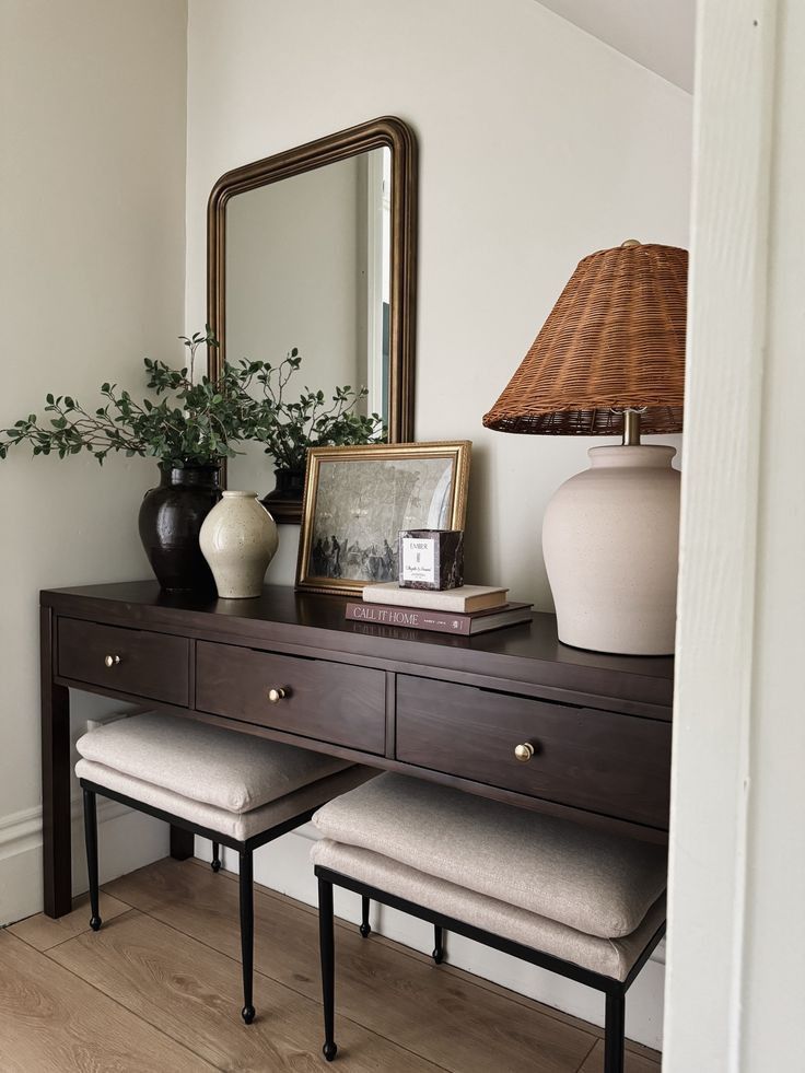 a dresser with two stools and a mirror on it's side, next to a lamp