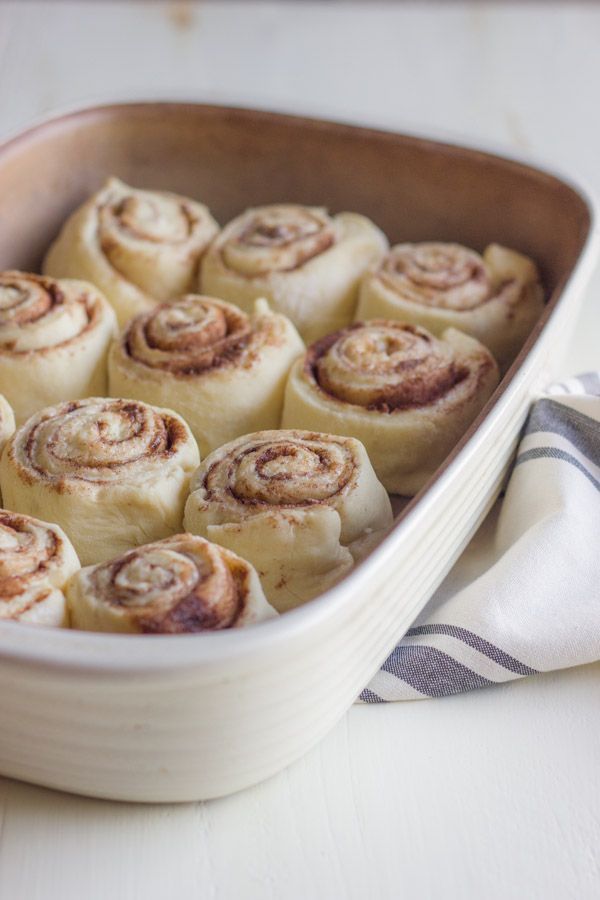 a baking dish filled with cinnamon rolls on top of a white tablecloth next to a towel