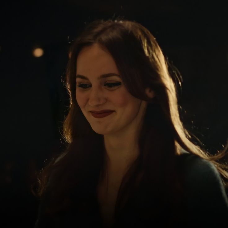 a woman with long brown hair smiling at someone in the dark, she is wearing a black dress