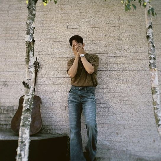 a man leaning against a wall with his hands to his face