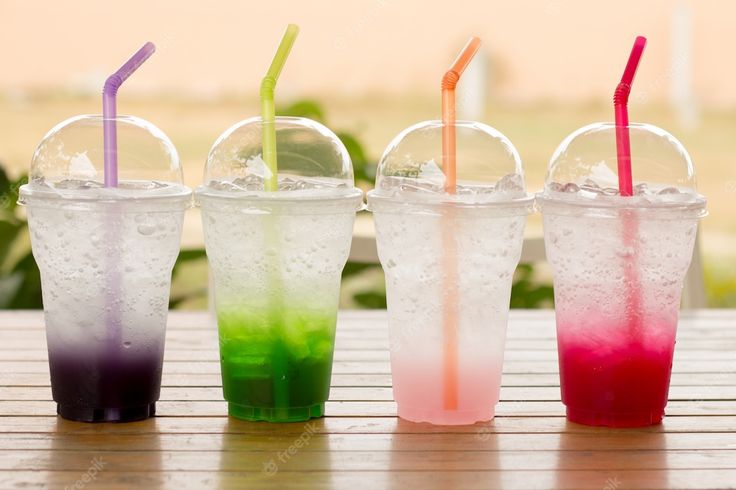 four different colored drinks are lined up on a table with their straws sticking out