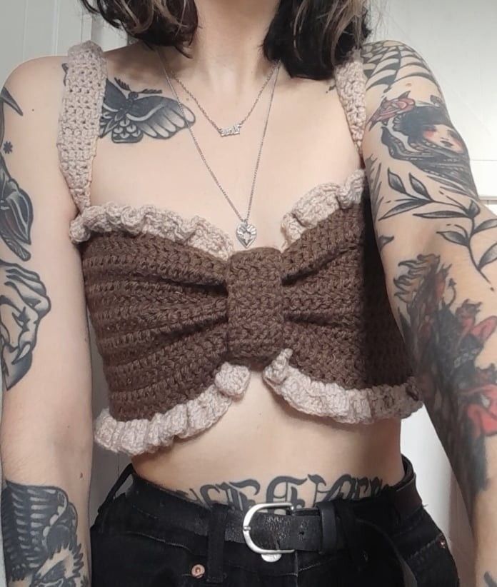 a woman with tattoos on her arms and chest wearing a brown bow tie crop top