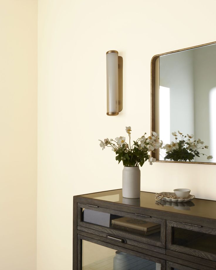 a vase with flowers sitting on top of a wooden table in front of a mirror