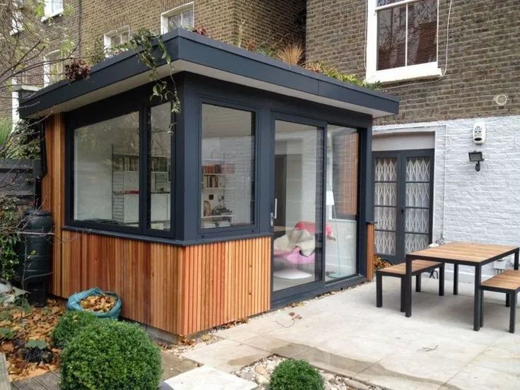 a small wooden building sitting in the middle of a yard next to a table and chairs