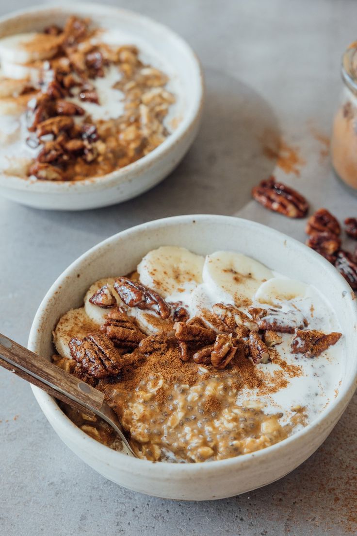 two bowls filled with oatmeal topped with bananas and pecans