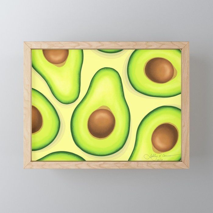 an avocado pattern on a yellow background framed in a wooden frame with a white wall behind it