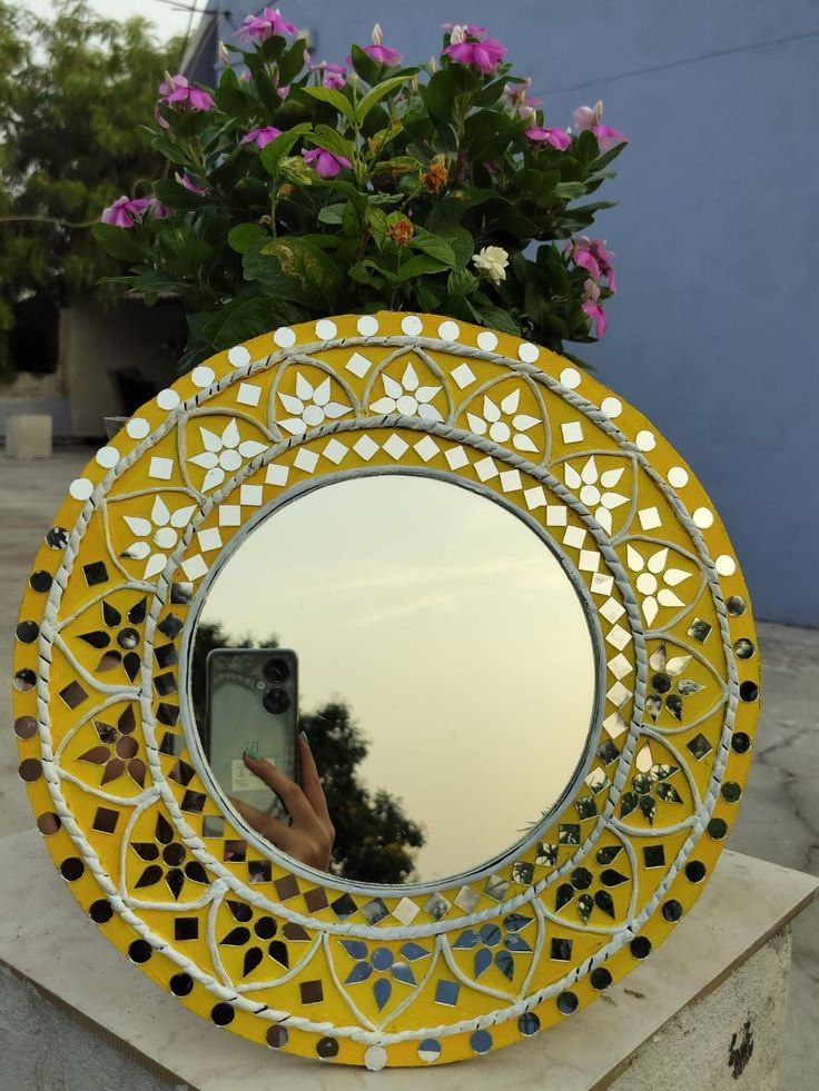 a yellow mirror sitting on top of a table next to a planter filled with flowers