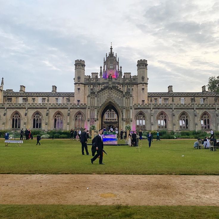 people are walking around in front of an old castle like building with tall towers and arched windows