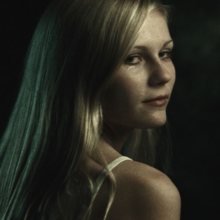 a woman with long blonde hair standing in front of a dark background and looking off to the side