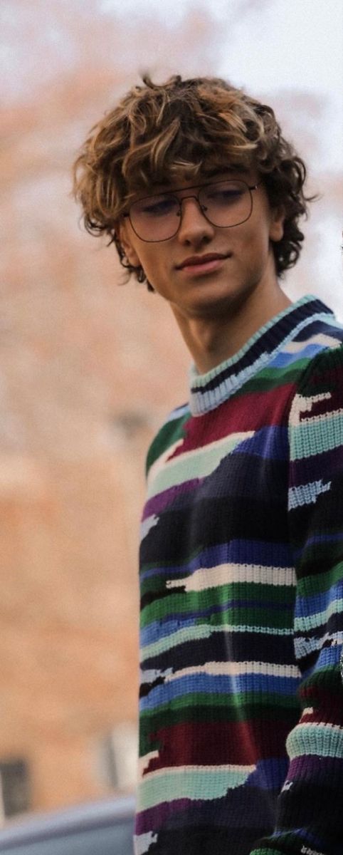 a young man with curly hair and glasses holding a cell phone