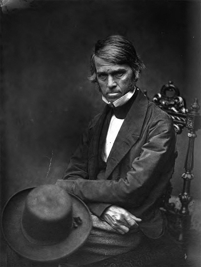 an old black and white photo of a man in a suit with a hat on his lap