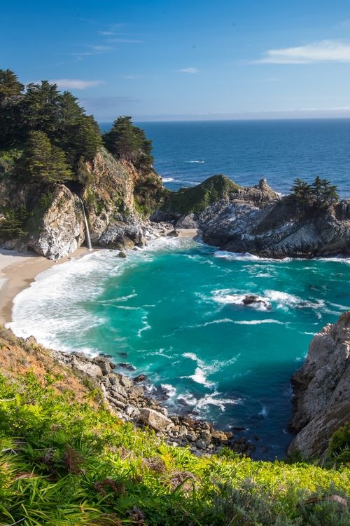 the ocean is blue and green with waves coming in from the rocks on the shore