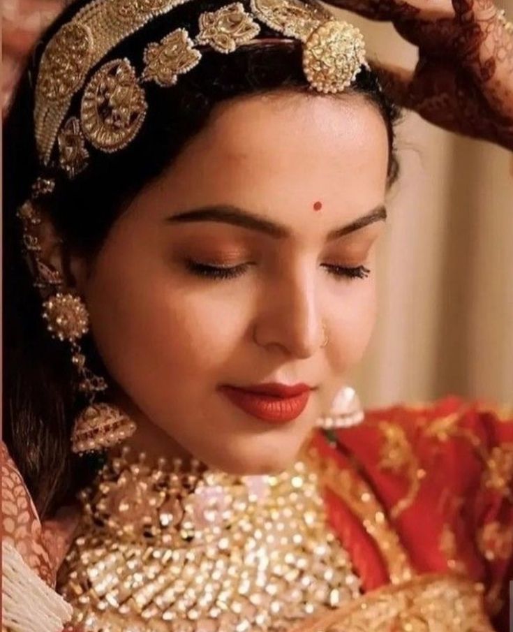 a woman wearing a gold and red bridal outfit with her hands on her head