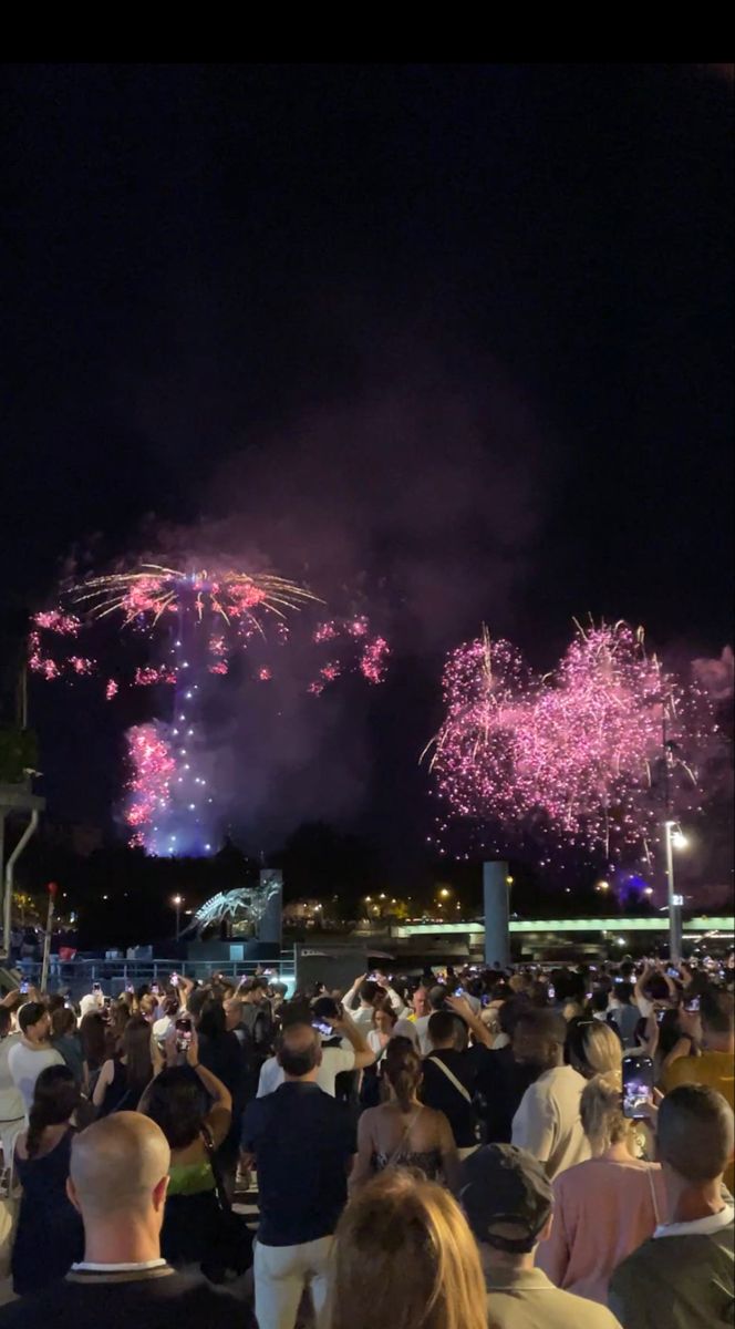 fireworks are lit up in the night sky above people sitting at tables and watching them