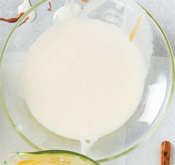 a glass bowl filled with white liquid next to a wooden spoon