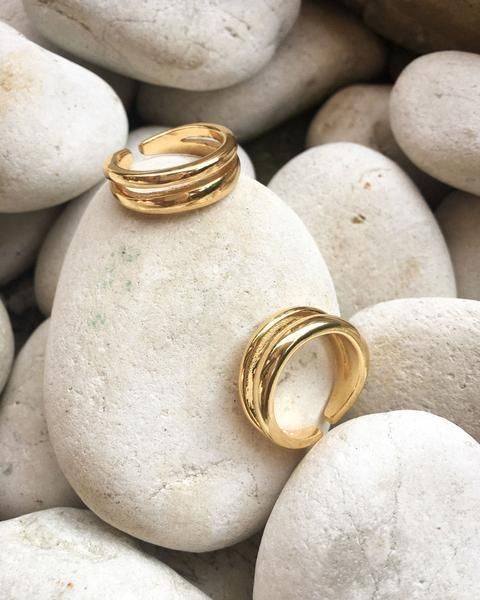 two gold rings sitting on top of white rocks next to each other, with one ring in the middle