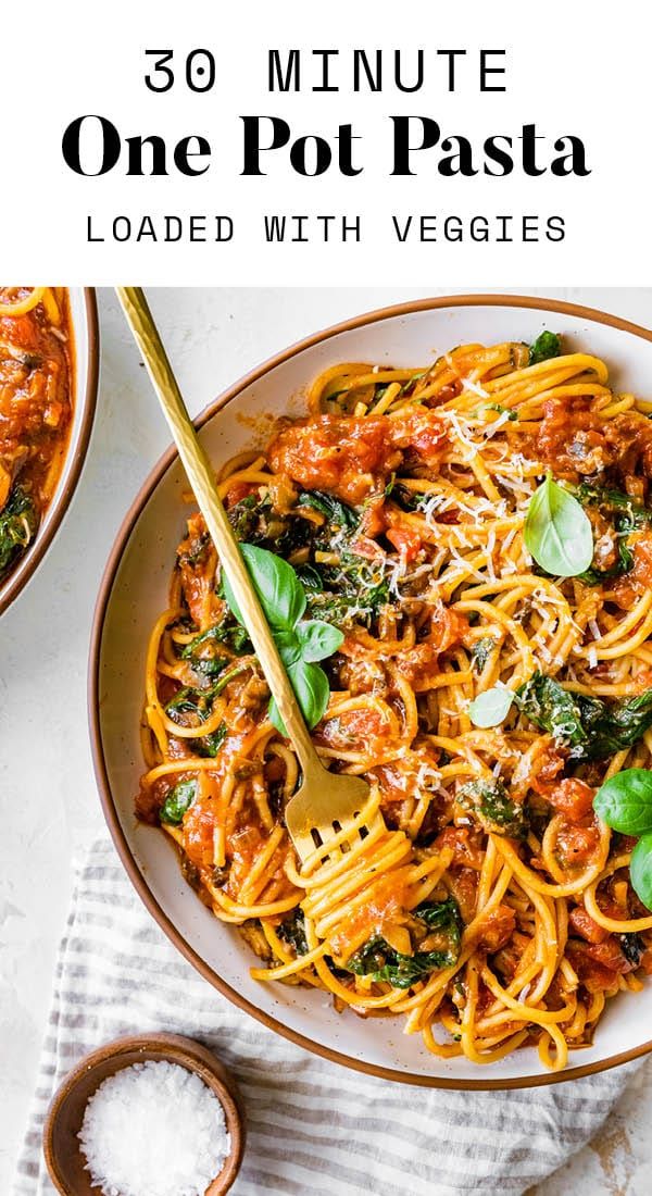 a bowl filled with pasta and spinach on top of a white table next to two bowls