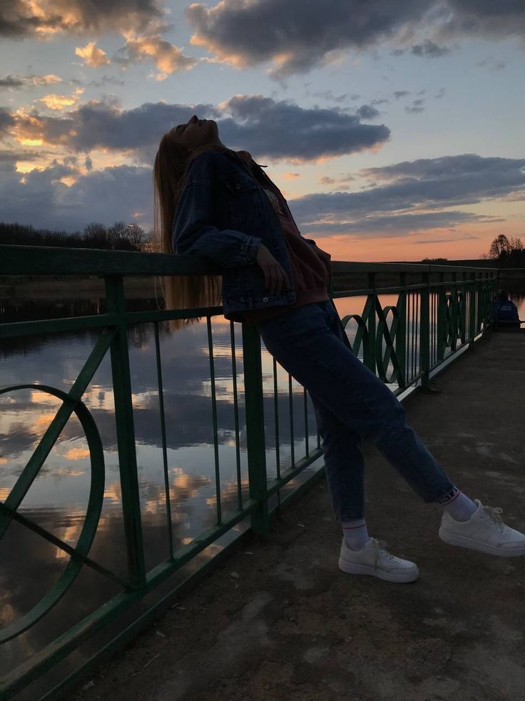 a woman leaning on a rail next to a body of water with clouds in the background