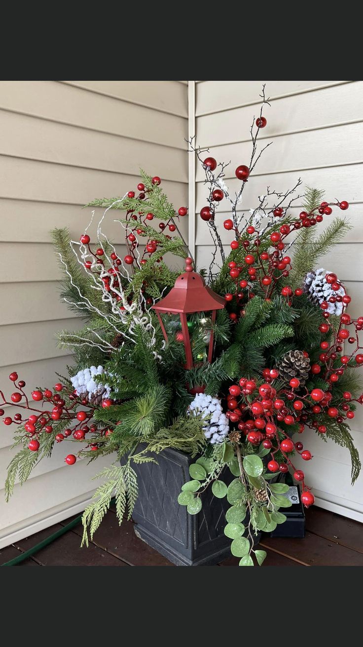 a potted plant with red berries and greenery on the side of a house