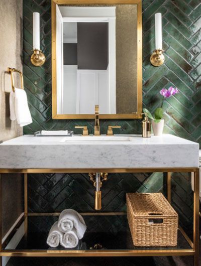 a bathroom with green tiled walls and gold fixtures, including a marble sink countertop