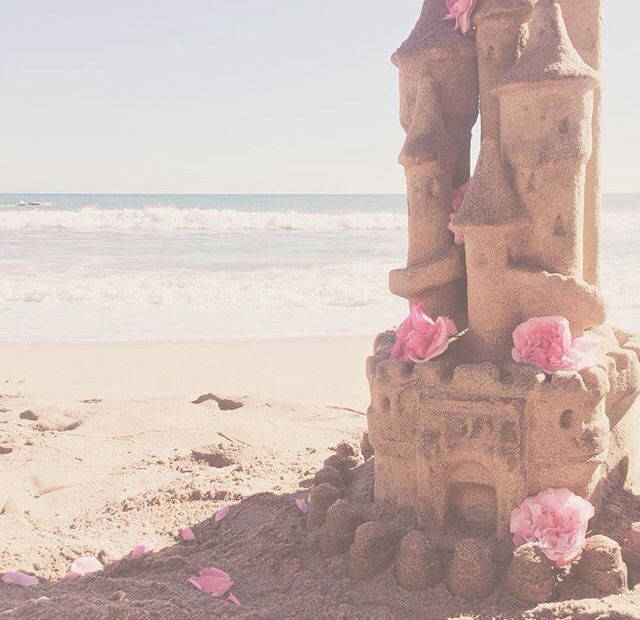 a sand castle with pink flowers on the beach