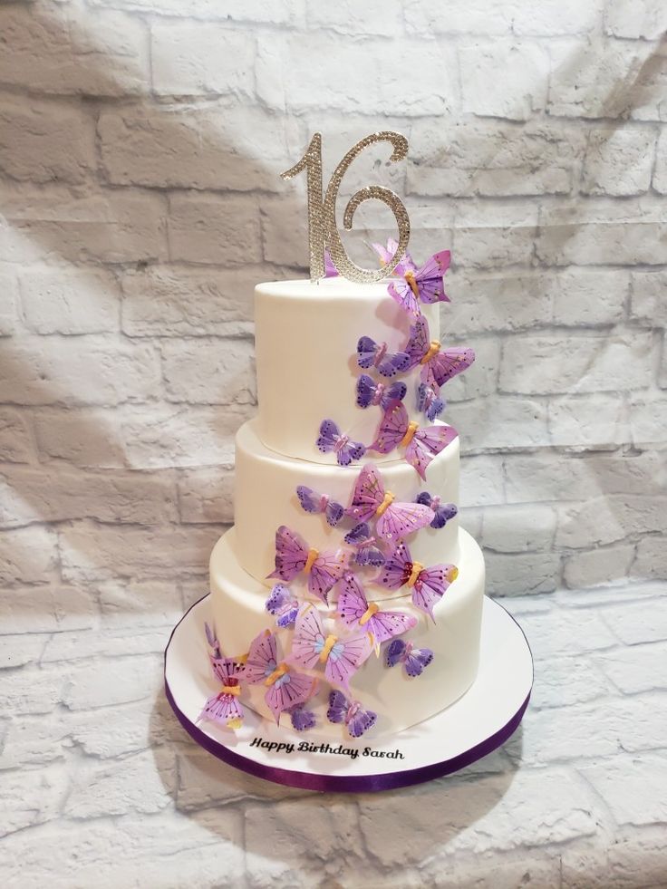 a white cake with purple butterflies on it and the number sixteen is displayed in front of a brick wall