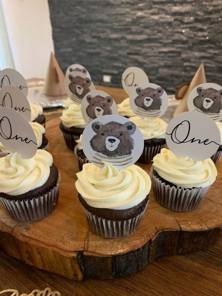 there are cupcakes that have been placed on top of a wooden board with bear decorations