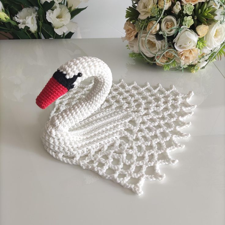 a crocheted swan sitting on top of a table next to white flowers and greenery