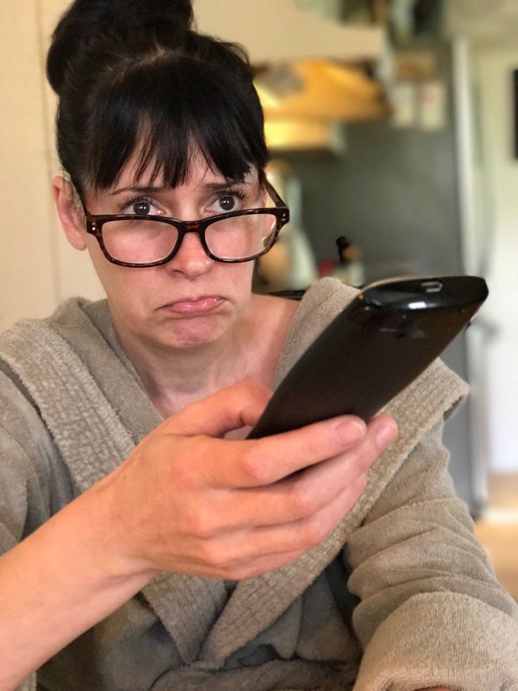 a woman wearing glasses looking at her cell phone while sitting in front of the camera