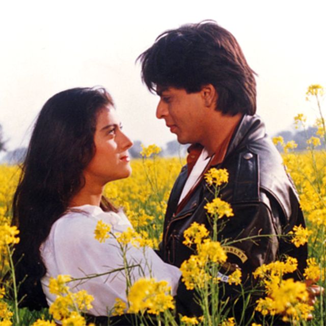 a man and woman standing in a field of yellow flowers looking at eachother