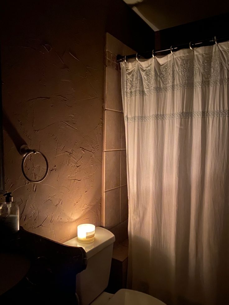 a white toilet sitting next to a bath tub under a bathroom mirror with a light on it