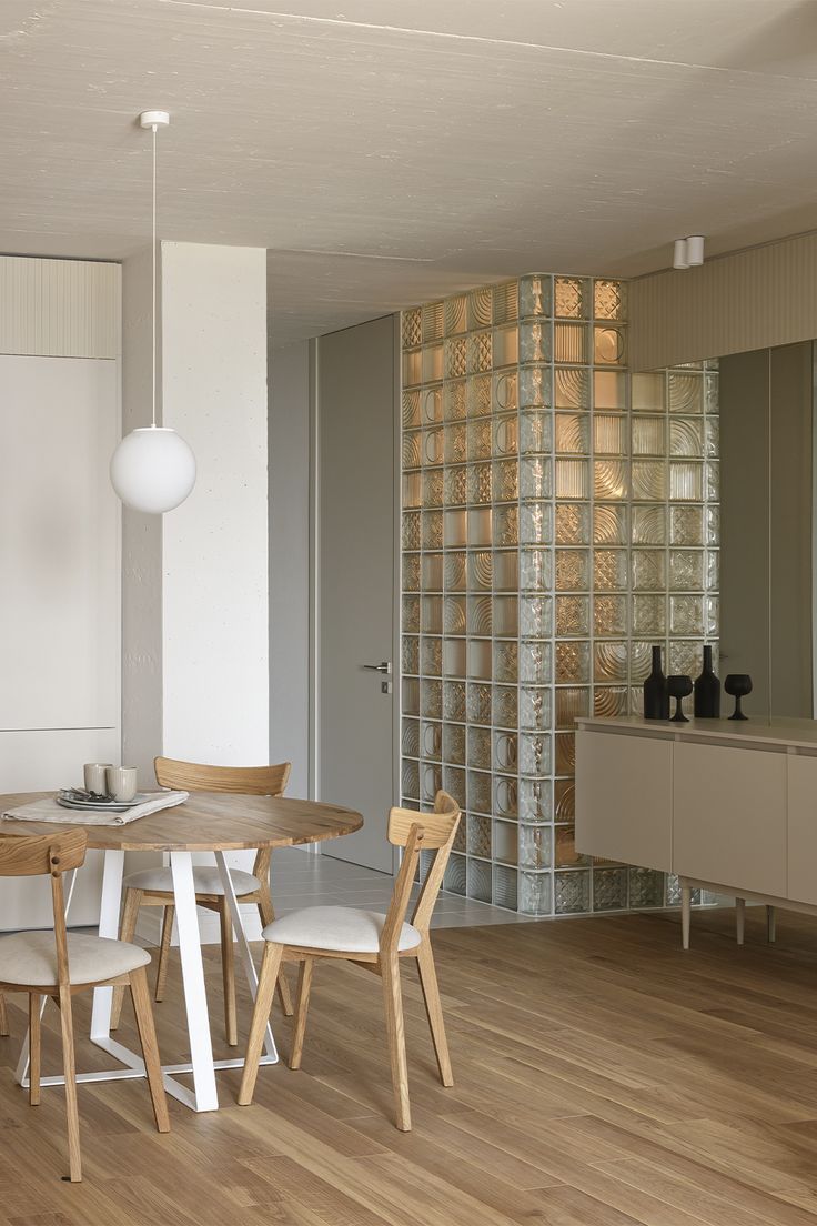 a dining room table with four chairs and a glass block wall in the back ground